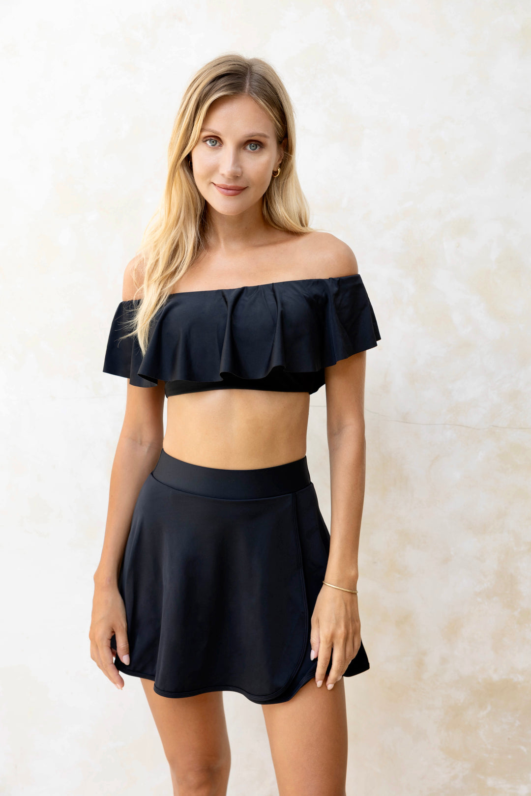 Front image of blonde girl standing wearing black high-waisted swim skirt with matching top